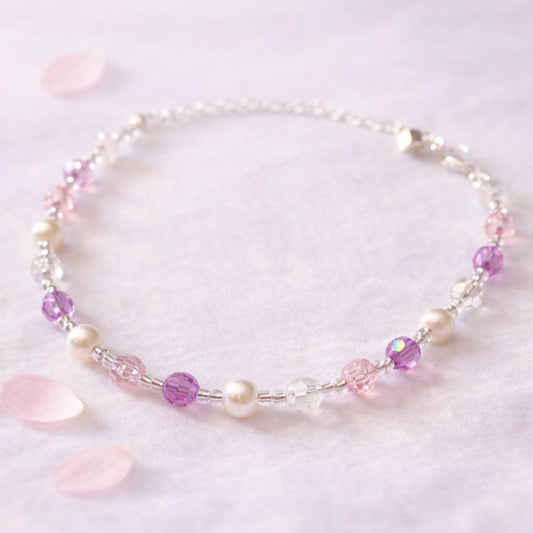 Pearl and pink, purple and clear crystal bracelet arranged on pale fabric with petals
